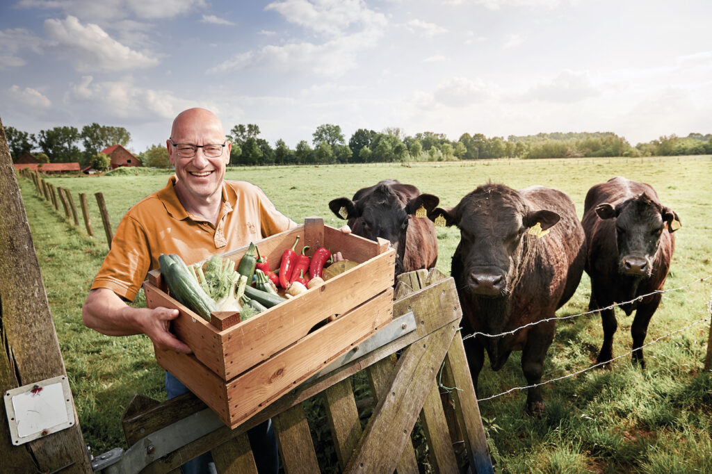 Oprichter van Je Leefstijl als Medicijn Wim Tilburgs met een kratje groente in de wei tussen de koeien